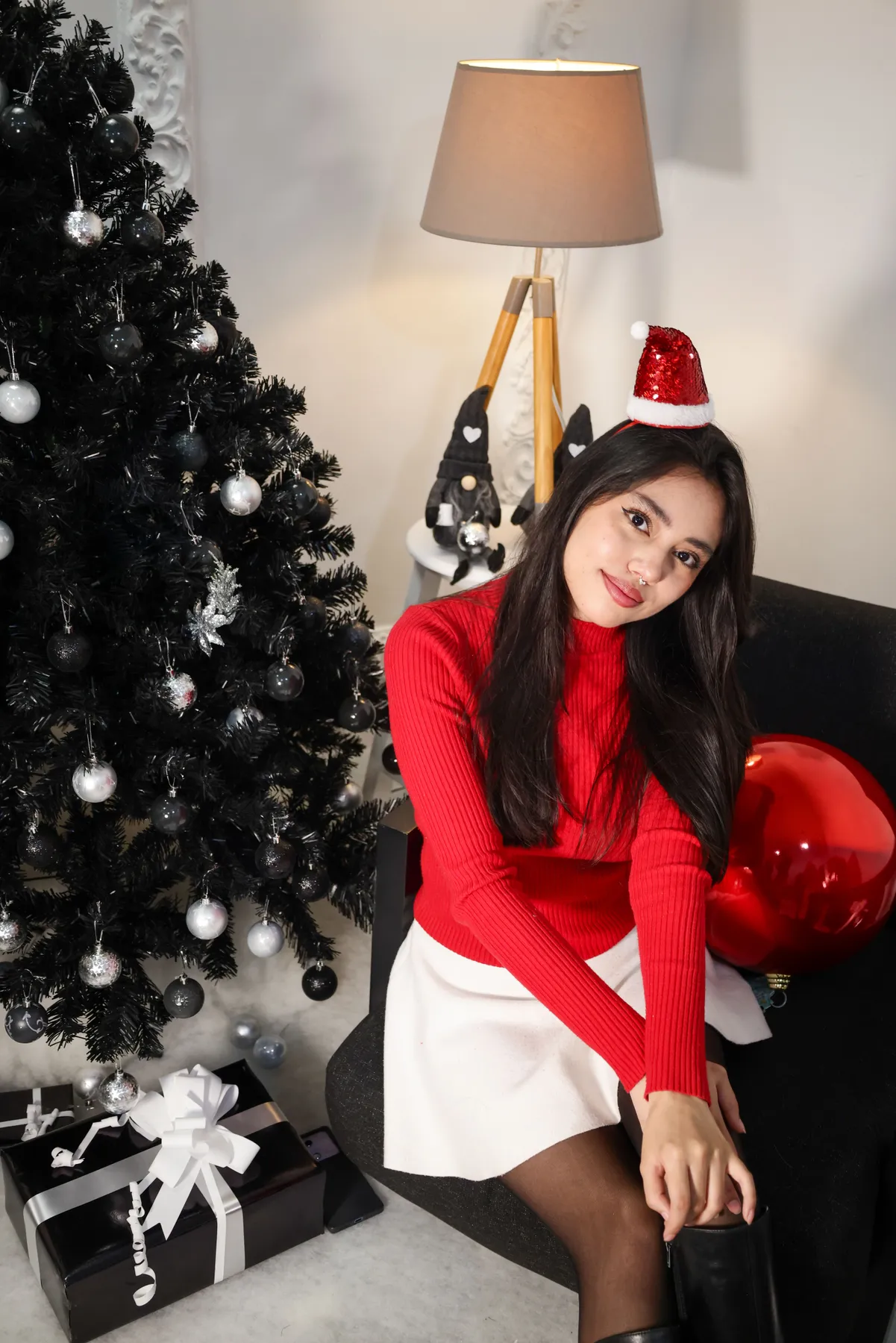 A cheerful woman in a Santa hat by a decorated tree, enjoying the festive holiday spirit.