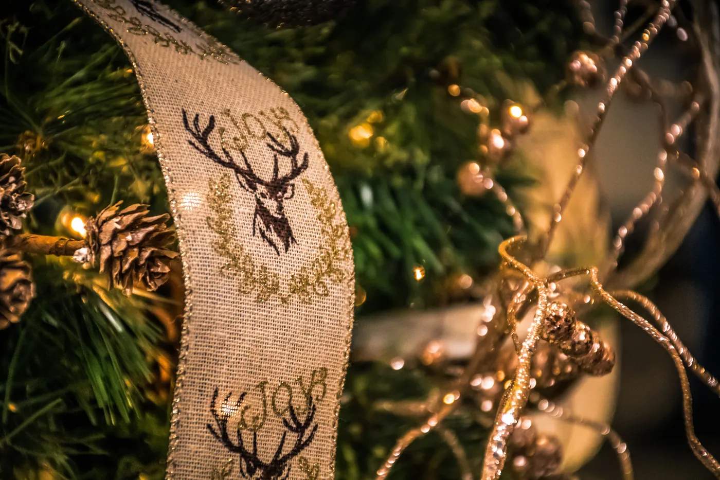 A detailed close-up of Christmas tree decorations featuring ribbons, lights, and pinecones.