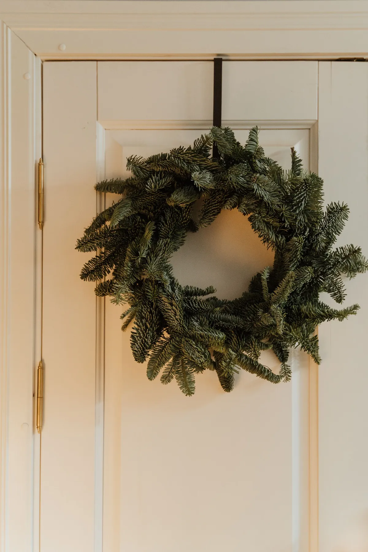 A lush green Christmas wreath hangs on a white door, exemplifying holiday decoration.