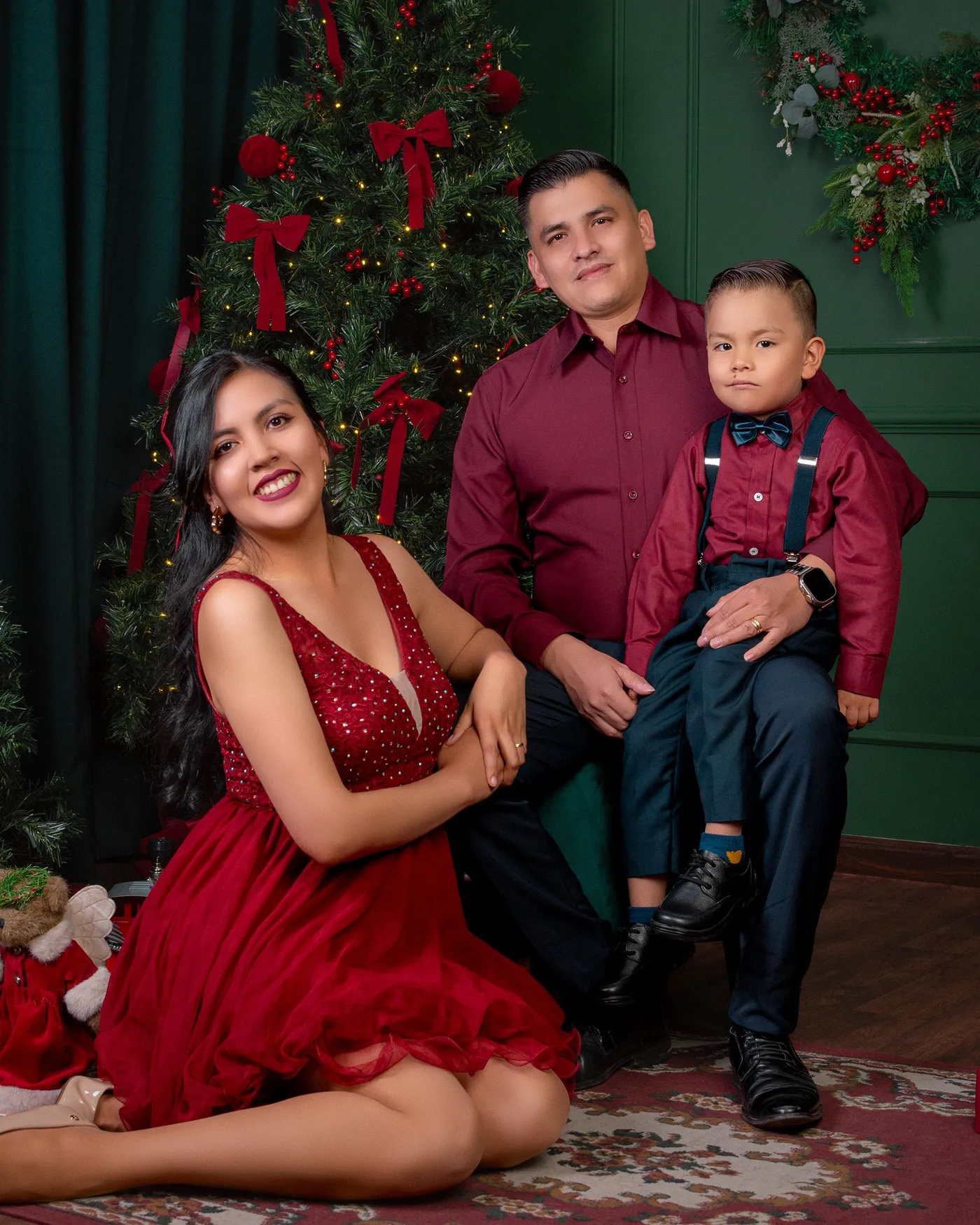 A smiling family poses in holiday attire by a decorated Christmas tree.