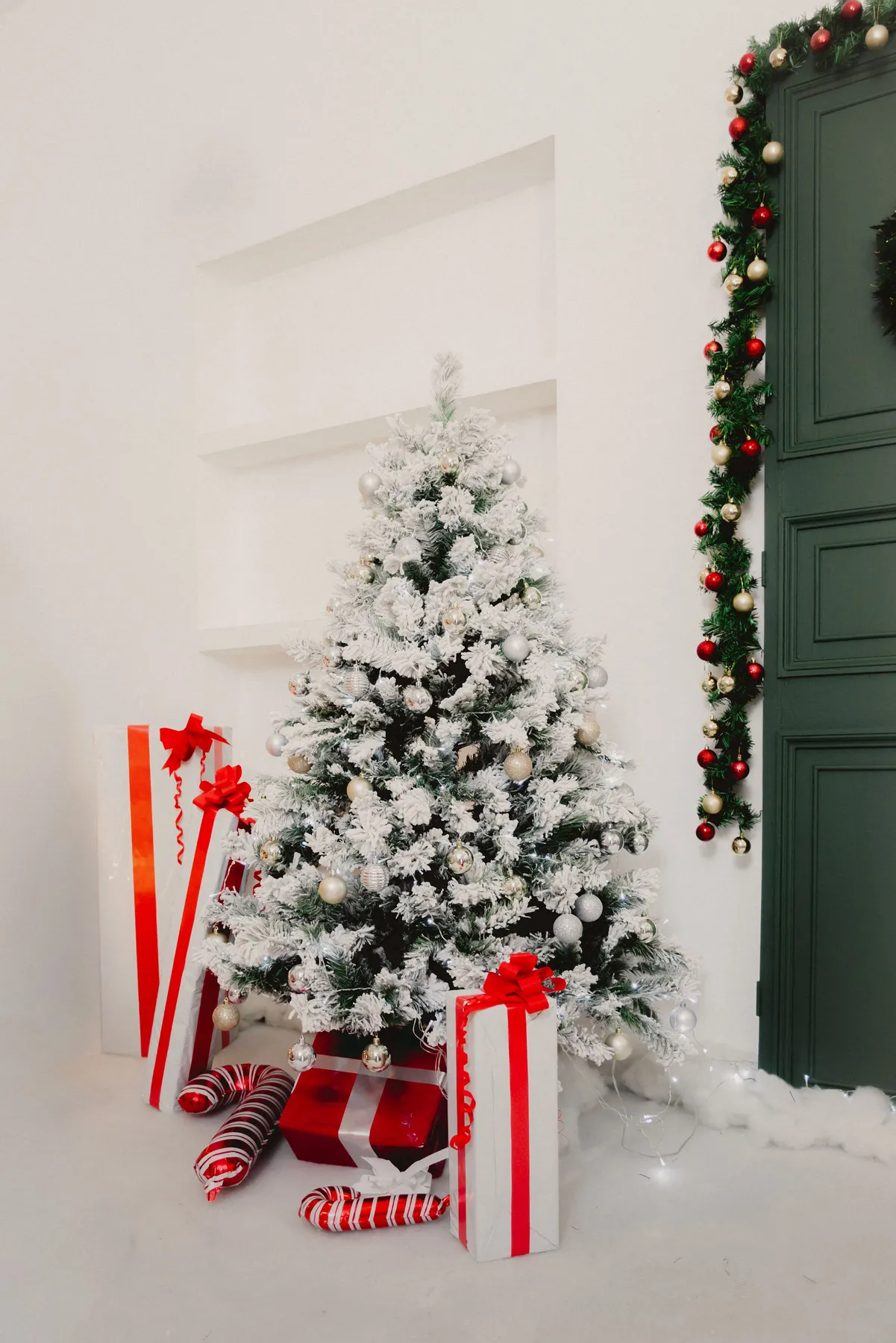 A snowy Christmas tree adorned with ornaments and surrounded by gifts in a festive indoor setting.