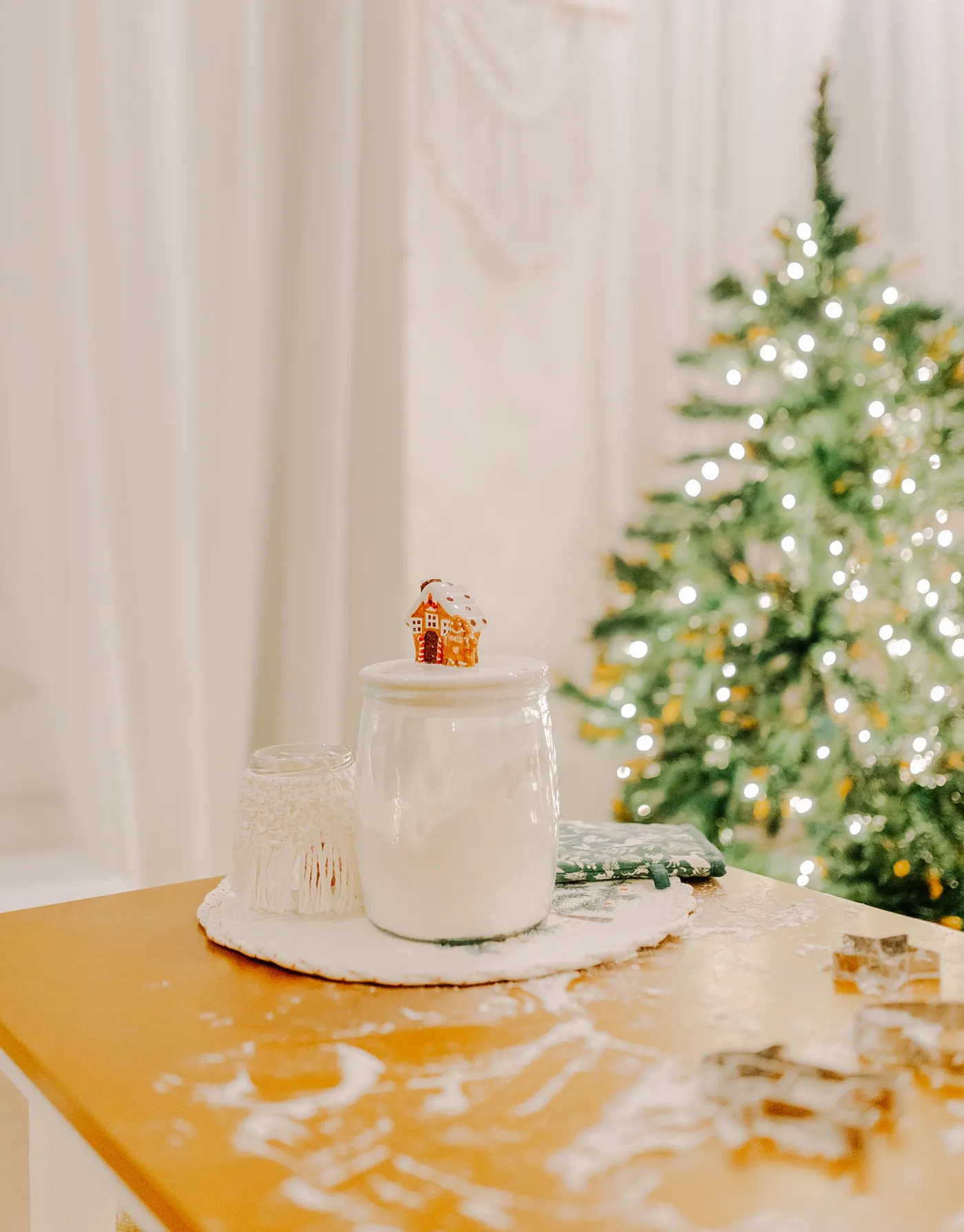 A warm indoor scene with a festive Christmas tree and kitchen decor featuring a porcelain jar and holiday accents.