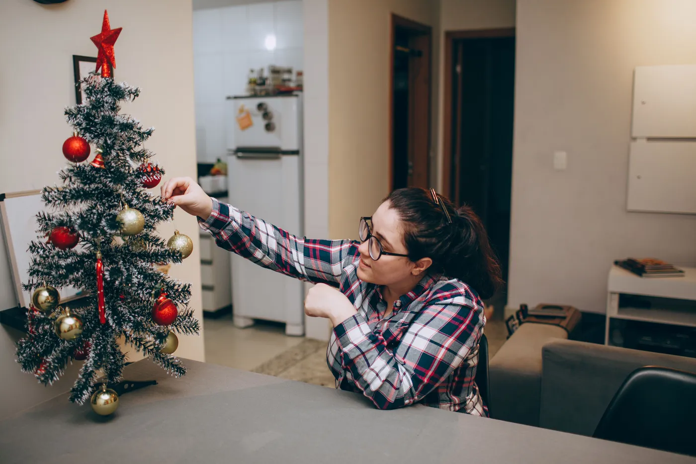 A woman decorates a small Christmas tree with ornaments in a cozy living room.