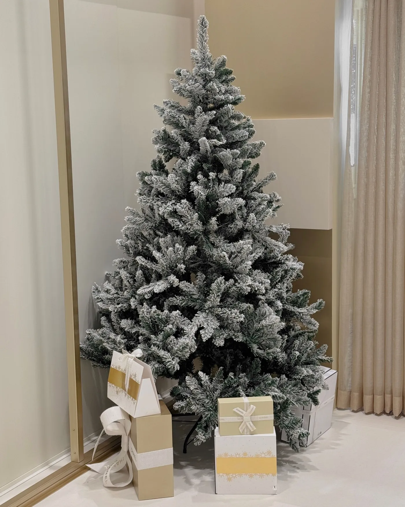 Beautiful frosted Christmas tree with elegant gift boxes in cozy indoor setting.