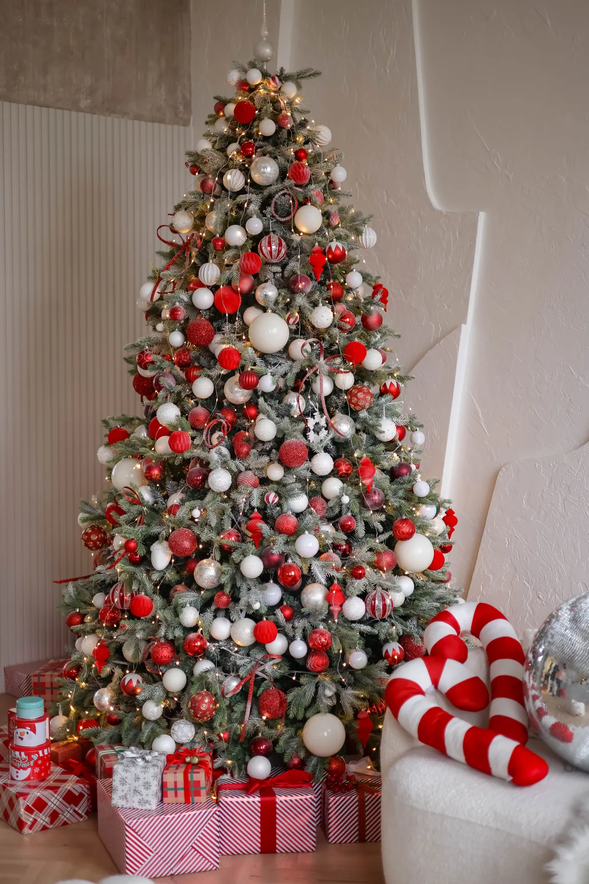 Beautifully decorated Christmas tree with gifts, red and white ornaments in a cozy room.