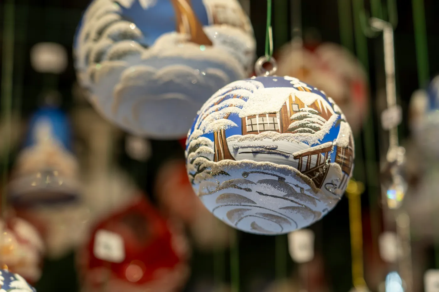 Blue Hand-Painted Christmas Ornament with Winter Cottage Scene A charming blue hand-painted Christmas ornament featuring a snowy winter cottage and frosted trees. This festive decoration captures the 