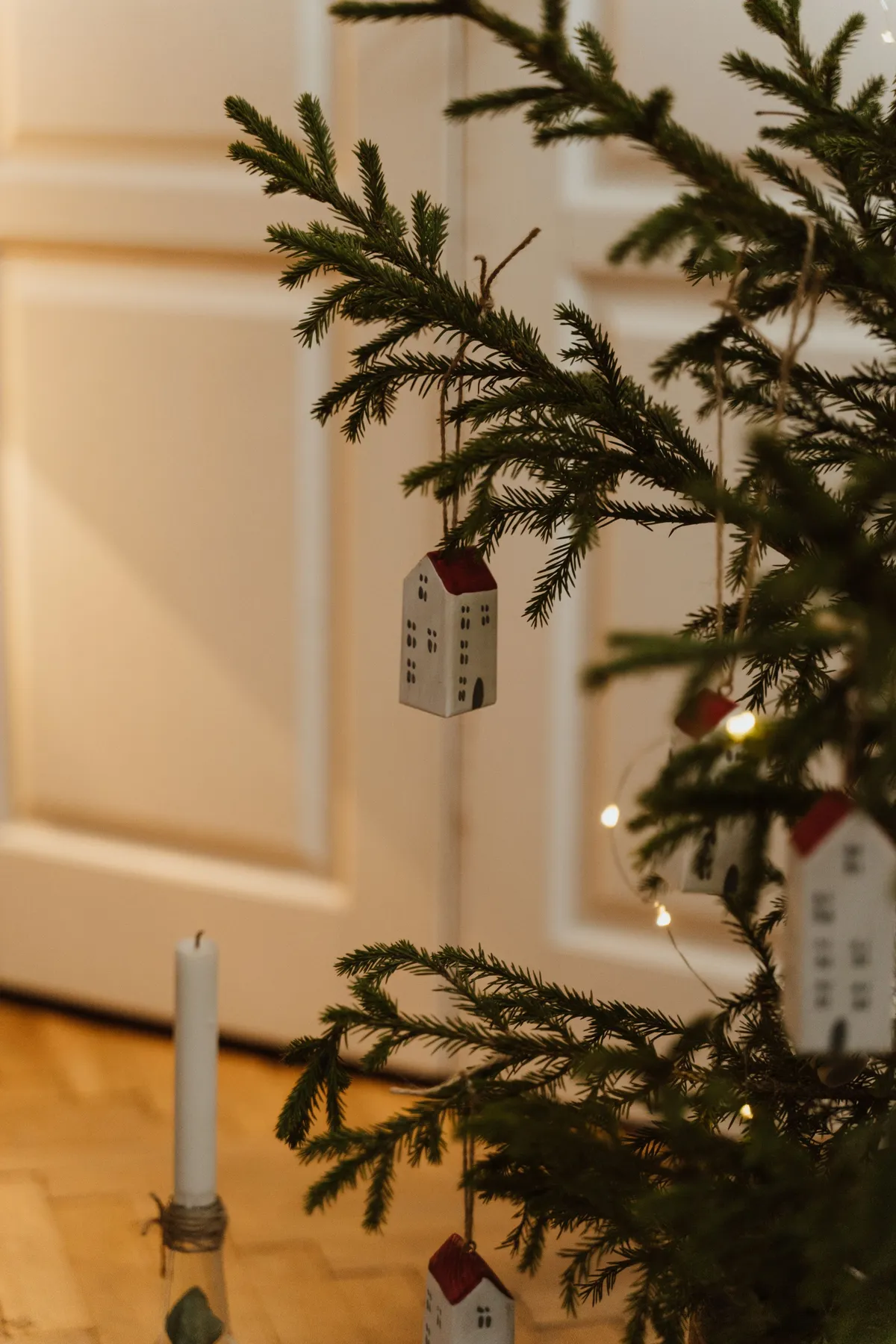 Christmas tree with small house ornaments and candle, creating a warm holiday ambiance indoors.