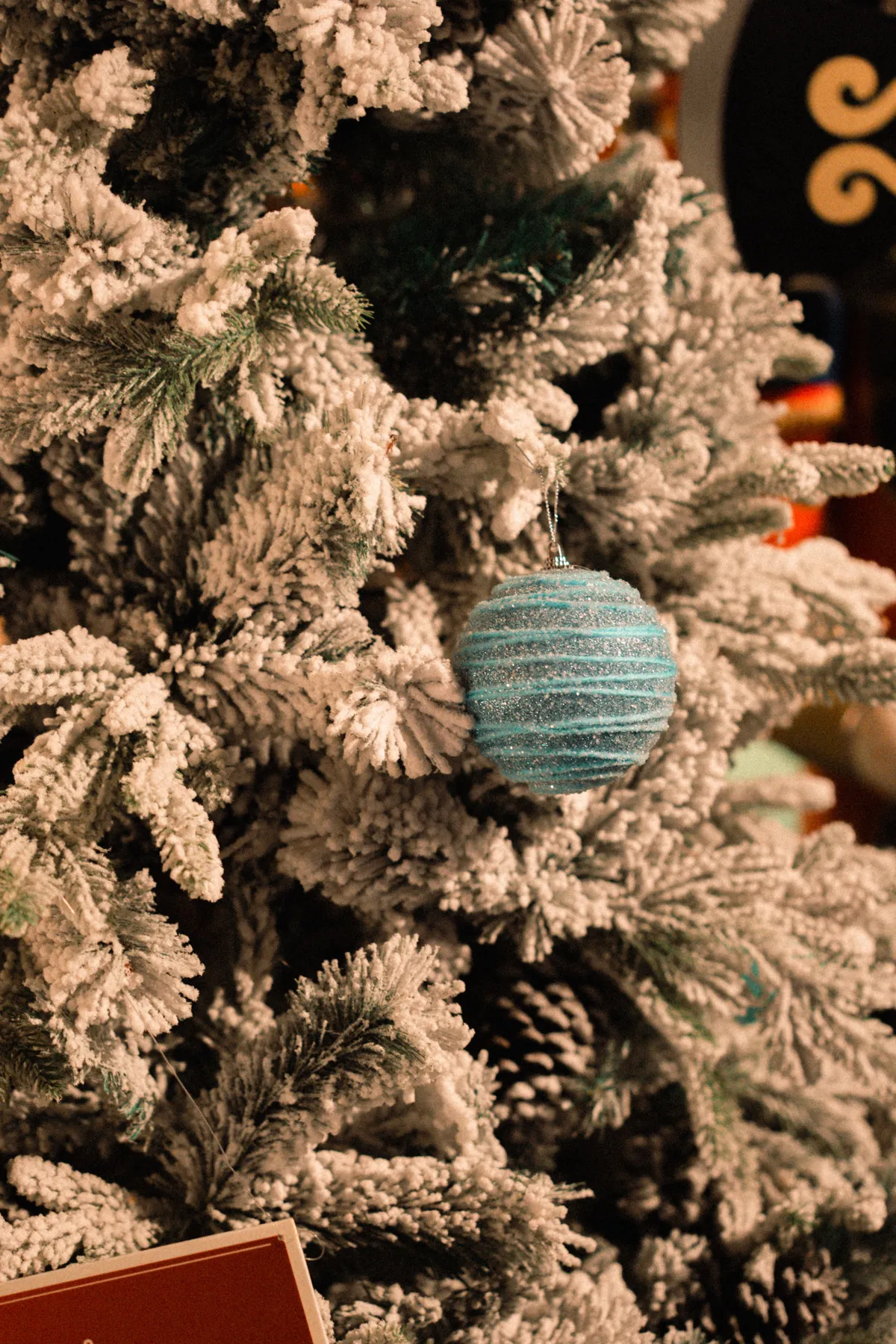 Close-up of a blue ornament hanging on a snow-covered Christmas tree, evoking a festive holiday mood.