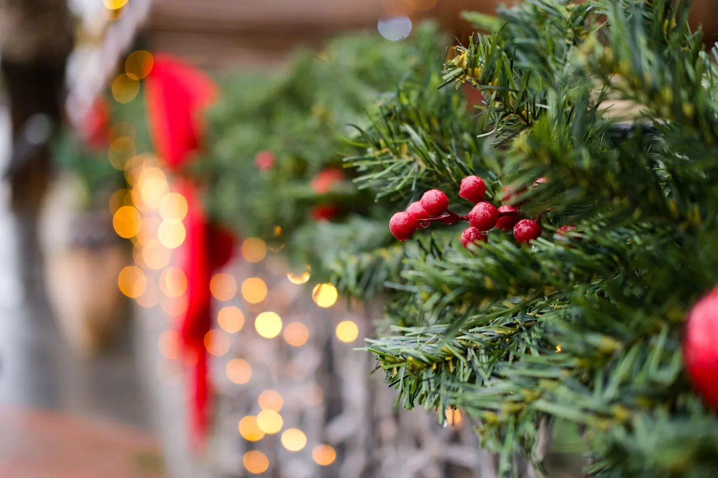 Close-up of a Christmas garland with red berries and glowing bokeh lights for a festive atmosphere.