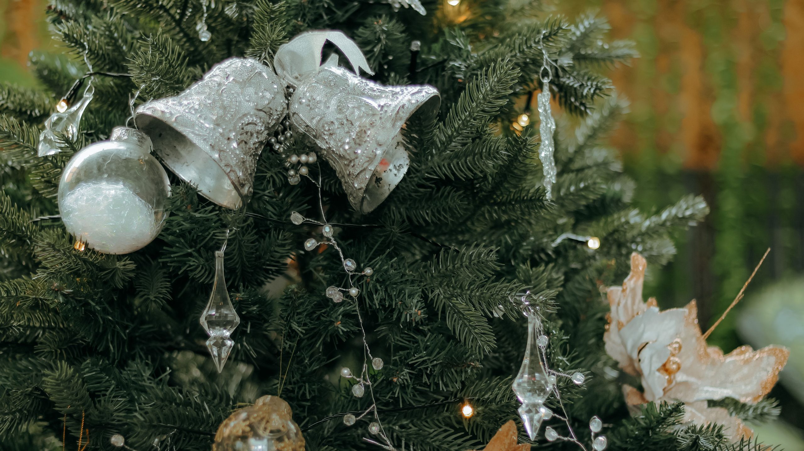 Close-up of a Christmas tree adorned with silver bells and glass ornaments, creating a festive mood.