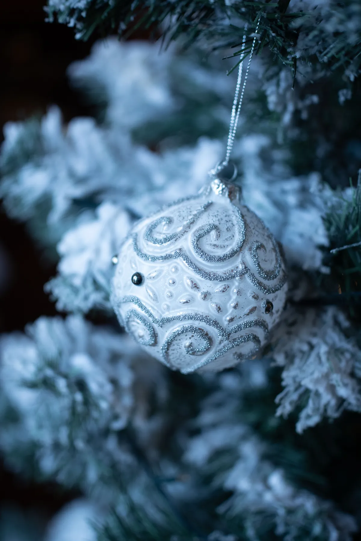 Close-up of a decorative white ornament on a frosted Christmas tree branch.