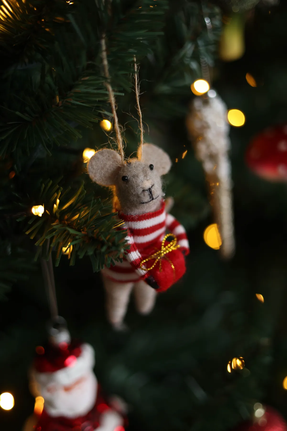 Close-up of a festive mouse ornament hanging on a Christmas tree with lights.