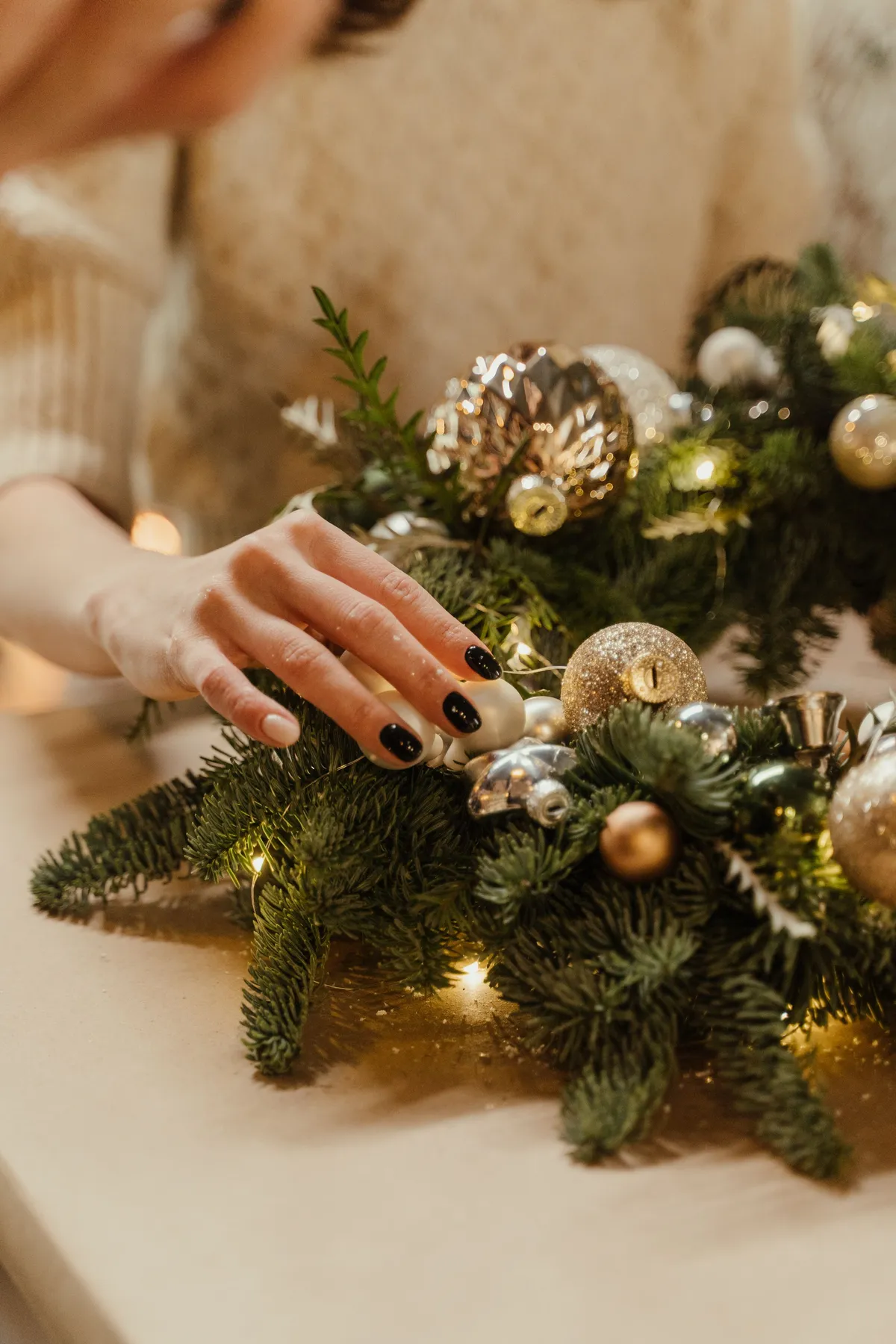 Close-up of a hand decorating a festive Christmas wreath with shiny baubles and lights indoors.