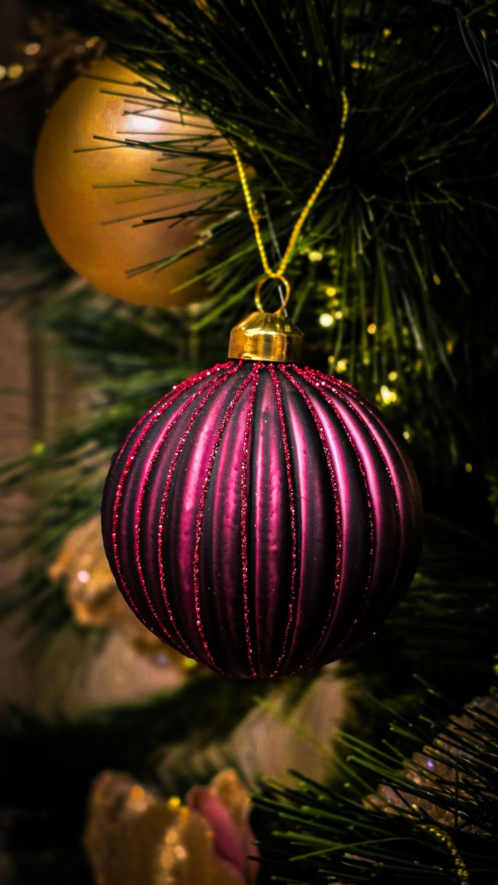 Close-up of a purple and gold Christmas ornament hanging on a holiday tree branch.
