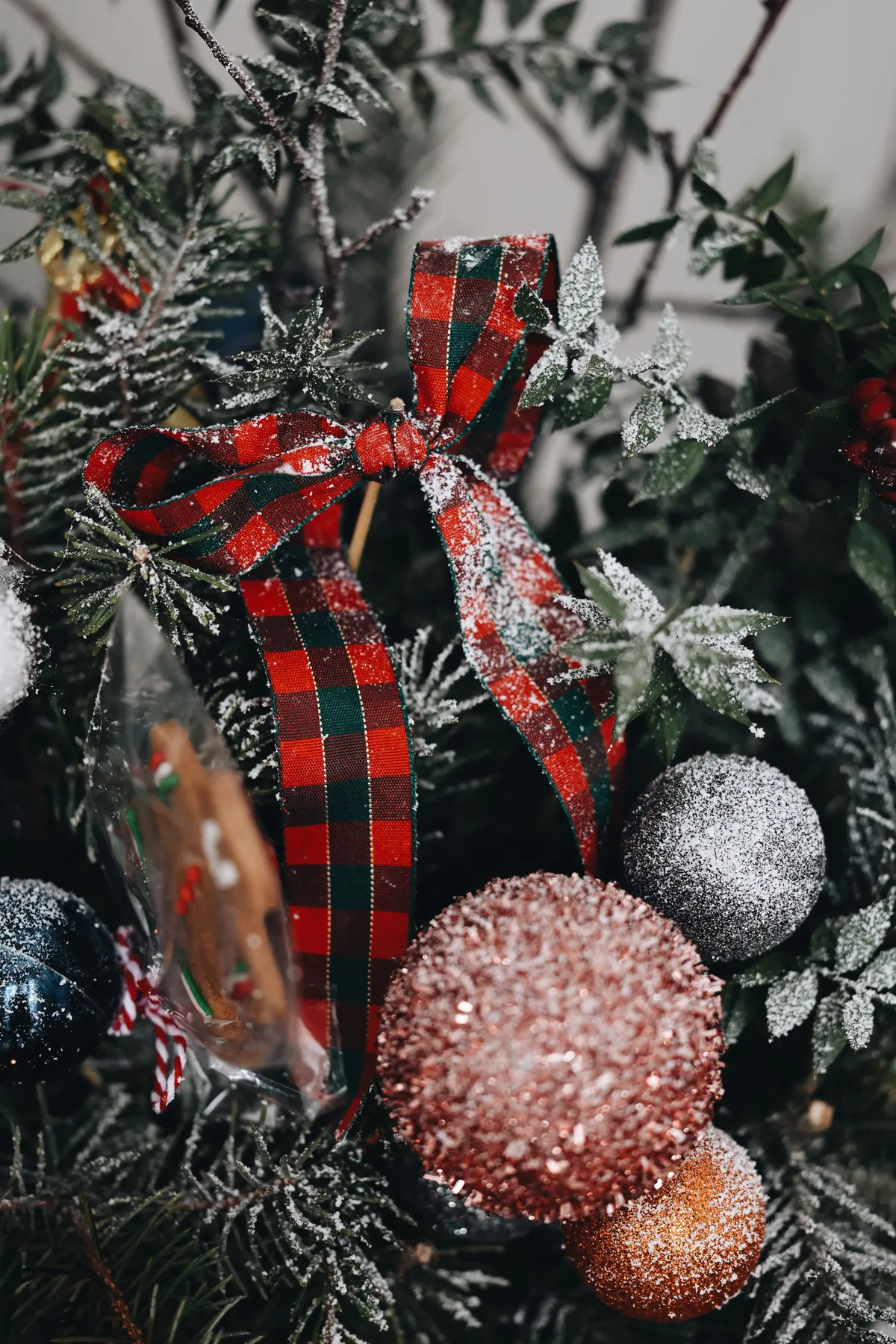 Close-up of Christmas tree with plaid ribbon and glittery ornaments, conveying festive spirit.