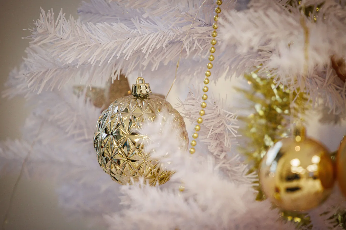 Close-up view of elegant gold ornaments hanging on a white Christmas tree with festive decorations.