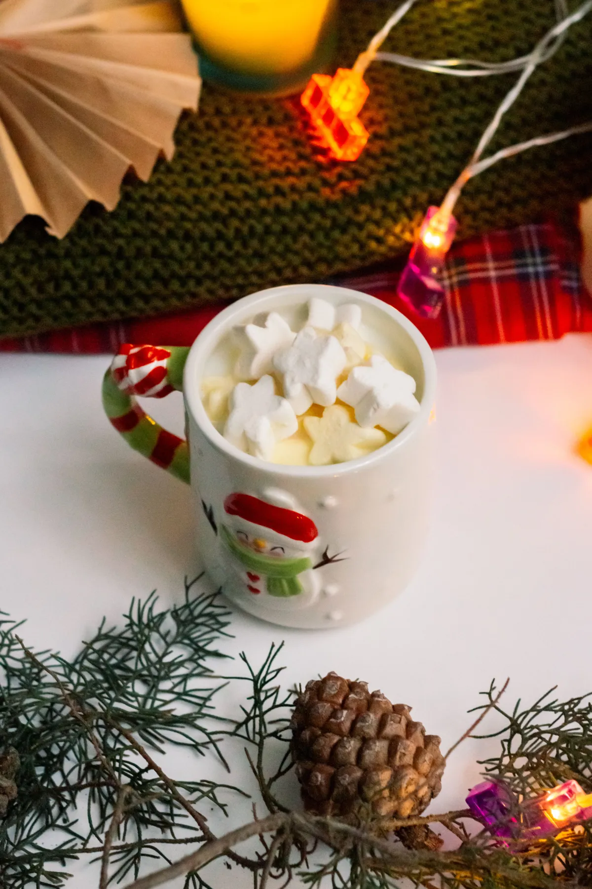 Cozy winter scene with hot chocolate in a snowman mug surrounded by festive decorations.