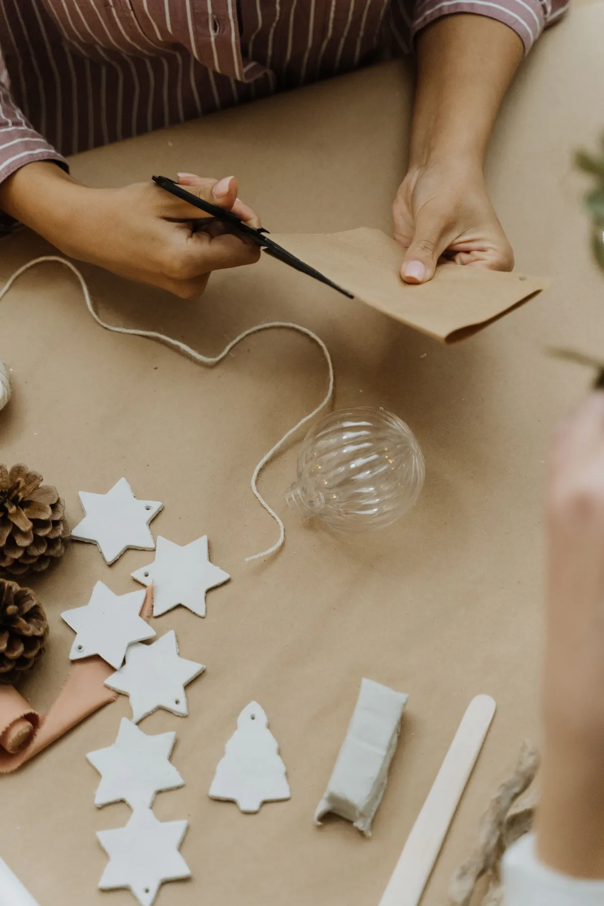 Crafting holiday decorations with paper, stars, and pinecones on a table.