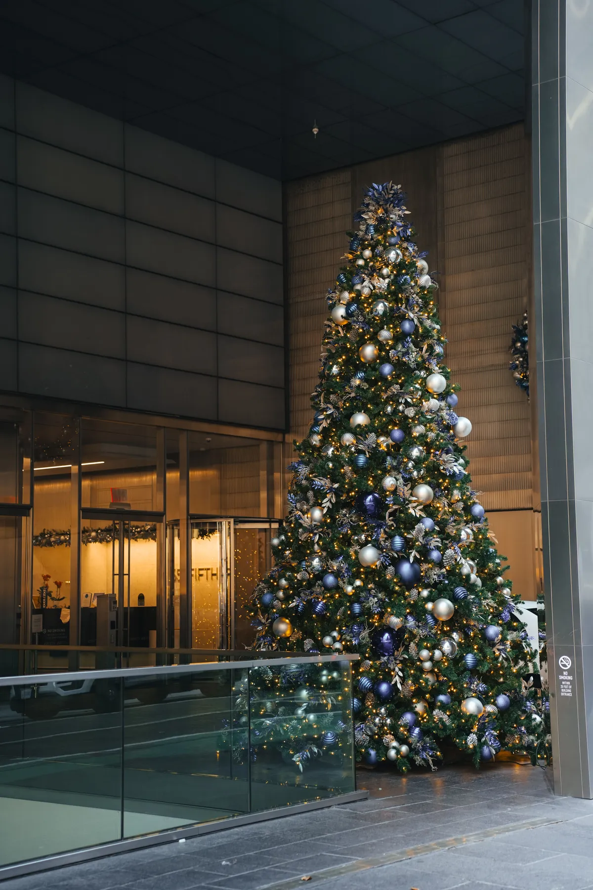 Elegant Christmas tree adorned with baubles in a modern urban lobby setting.