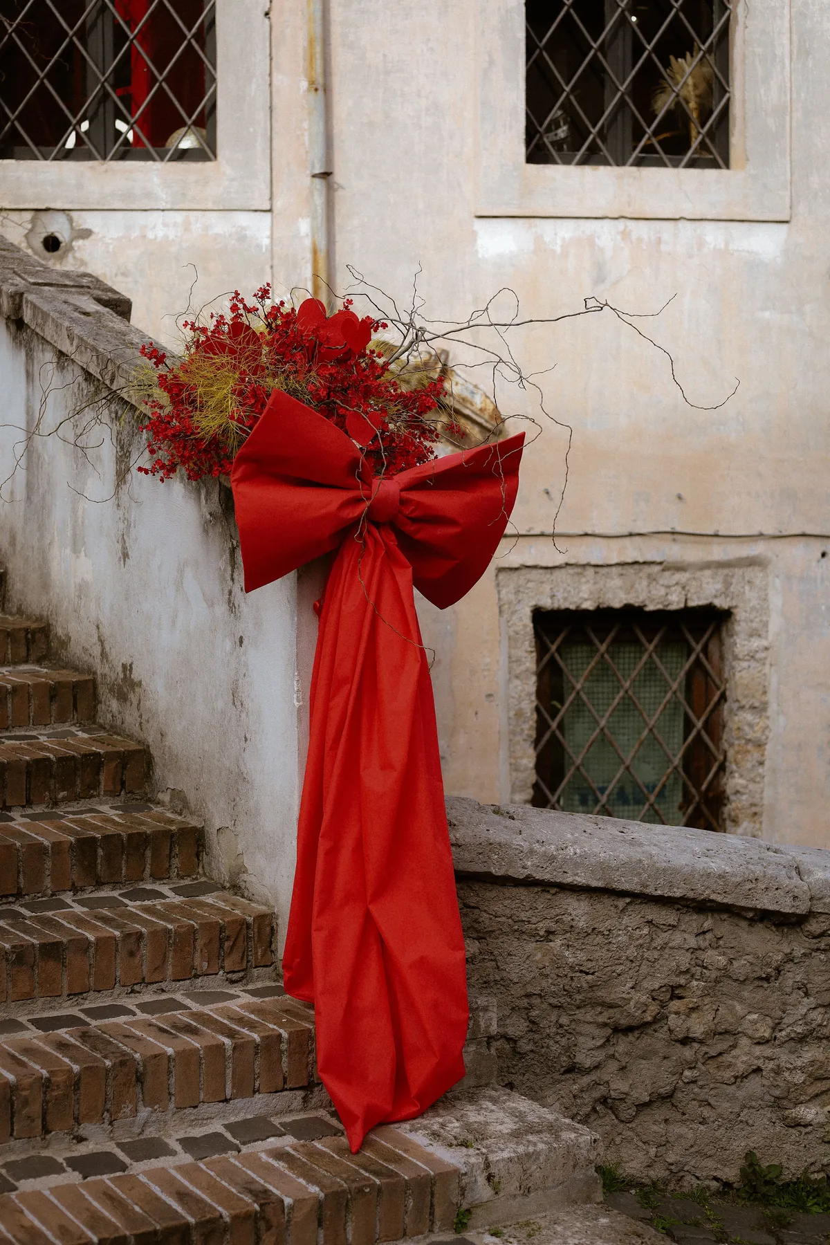 Elegant red ribbon and flowers adorn a vintage staircase, creating a festive atmosphere.