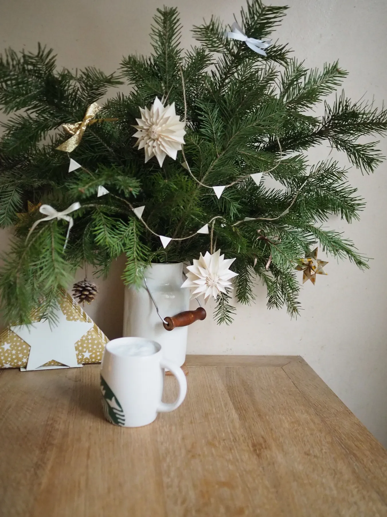 Festive Christmas arrangement with evergreen branches, ornaments, and a mug on a wooden table.