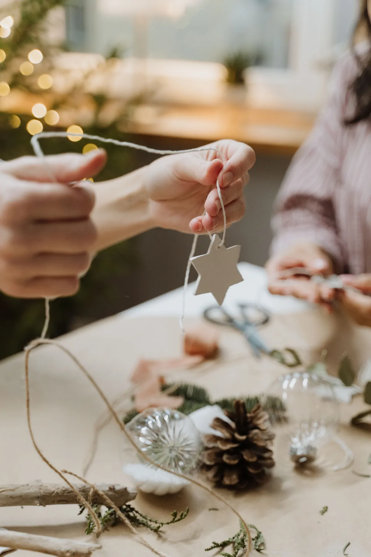 Hands crafting Christmas ornaments like stars and pinecones indoors.