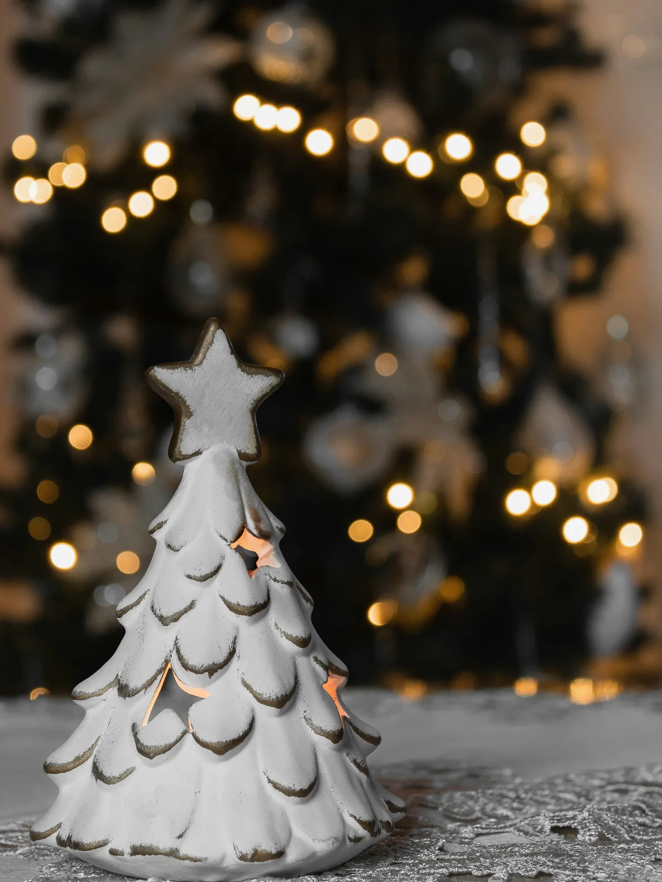 Little tree with candle inside with christmas tree in the background