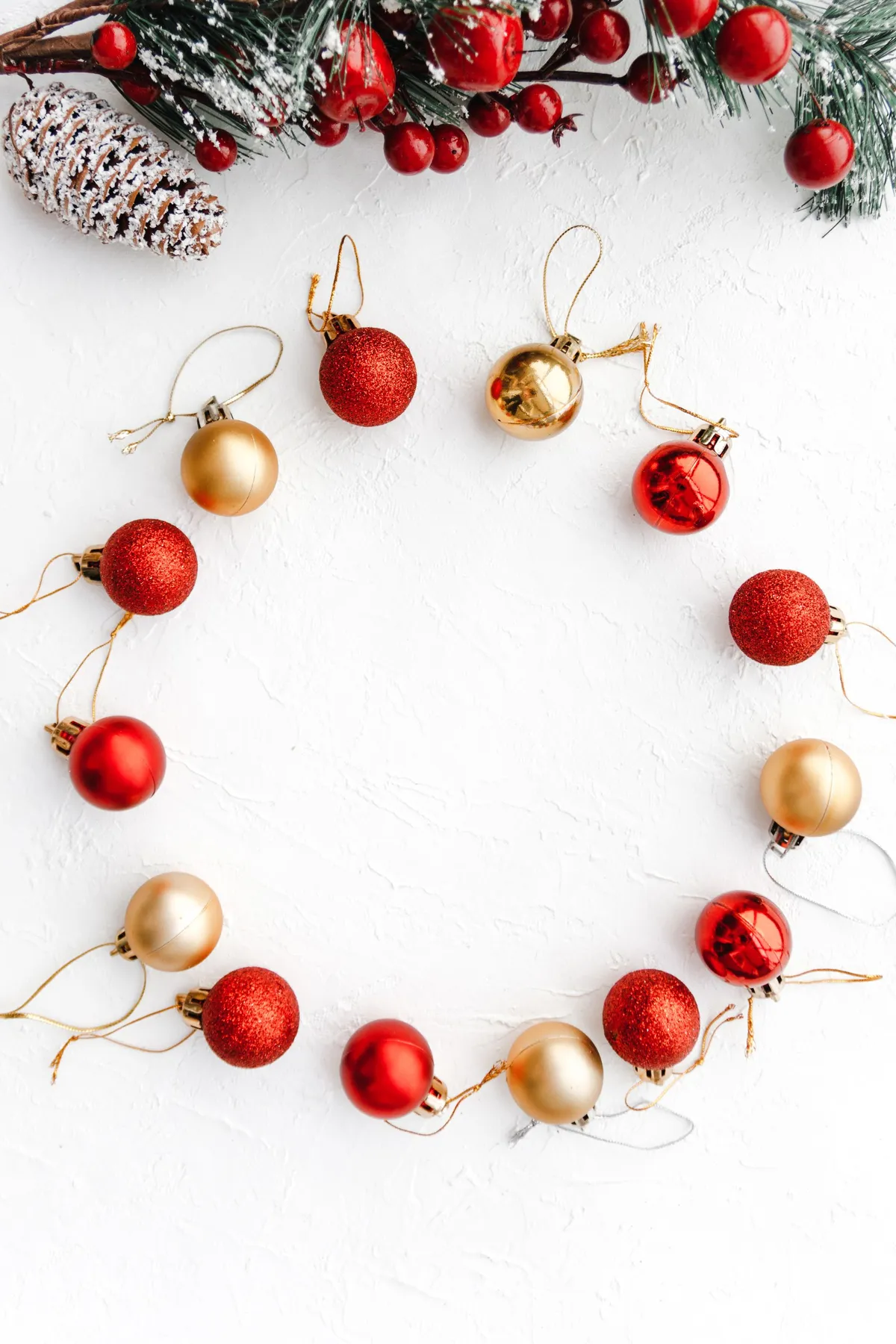 Red and gold Christmas baubles arranged in a circle on a white surface with holiday greenery.