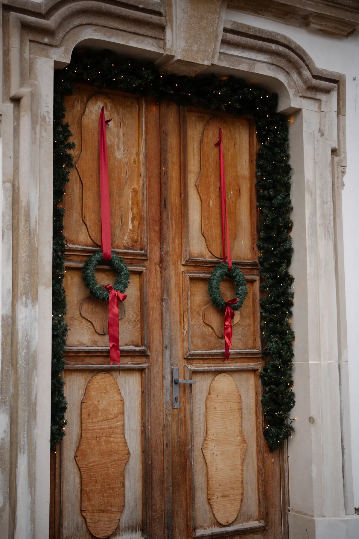 Rustic wooden door adorned with Christmas wreaths and red ribbons, creating a festive ambiance.