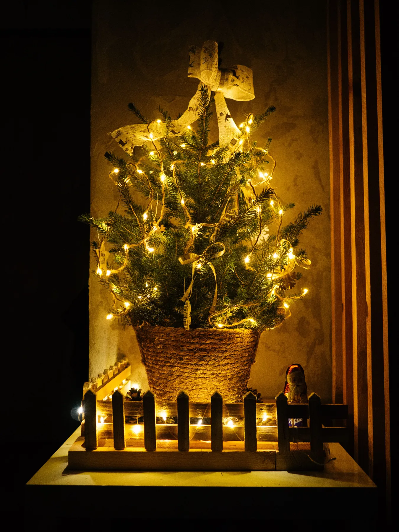 Small decorated Christmas tree with warm lights inside home, creating a cozy holiday atmosphere.
