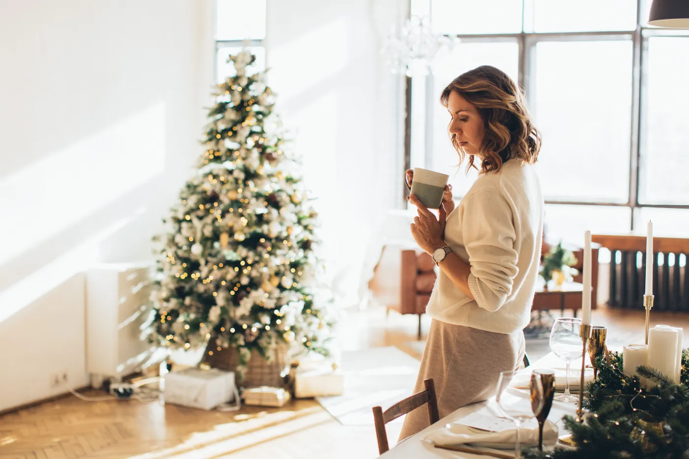 Woman enjoying coffee by a Christmas tree in a warm, festive indoor setting.